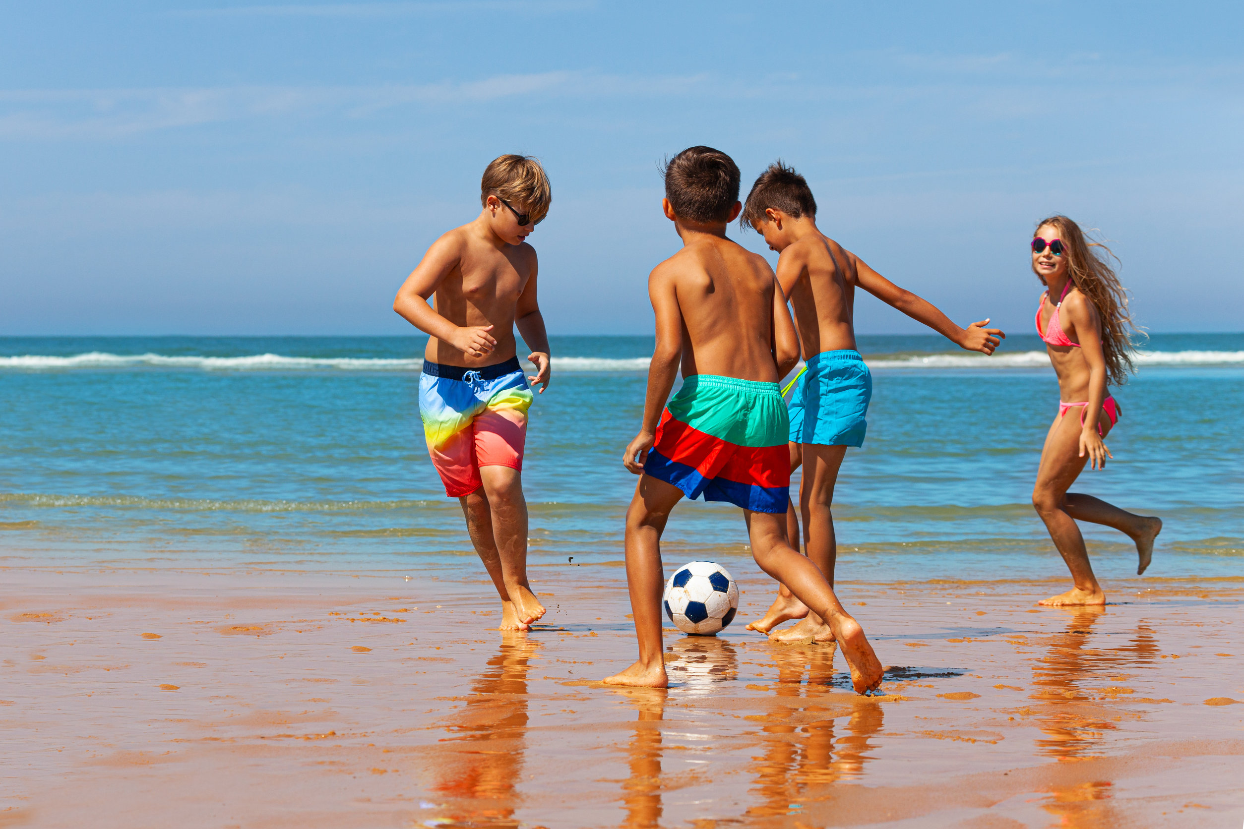 4 kids playing soccer on beach