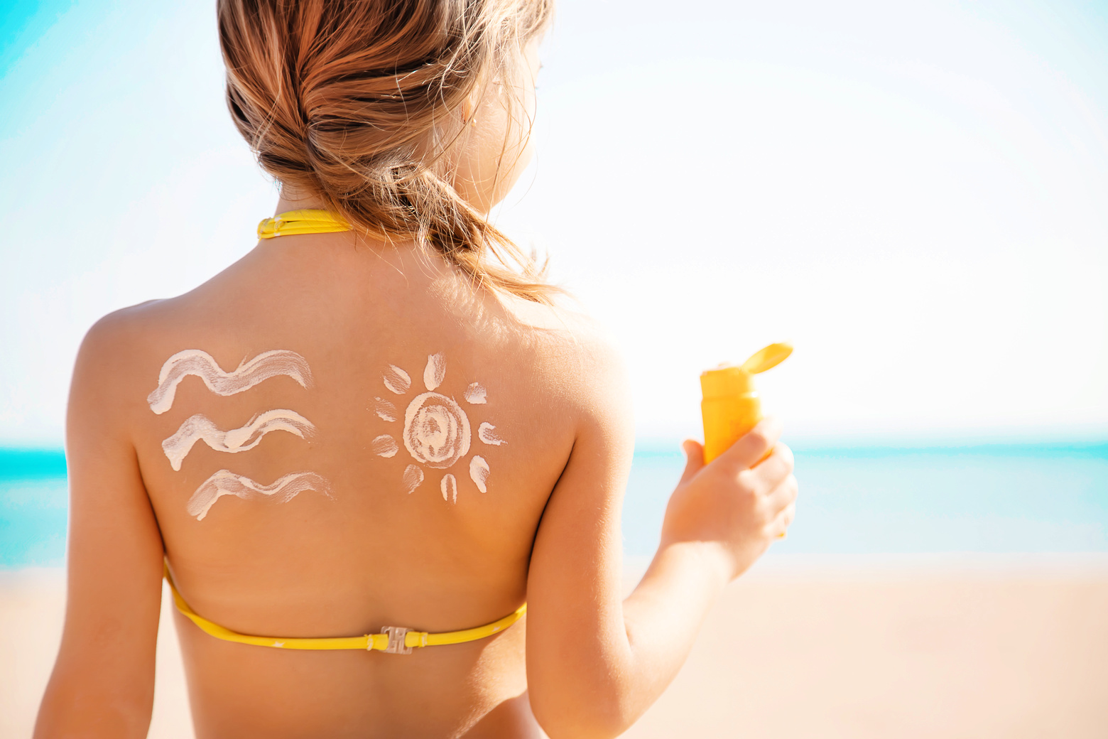 young girl at beach with sunscreen on her back